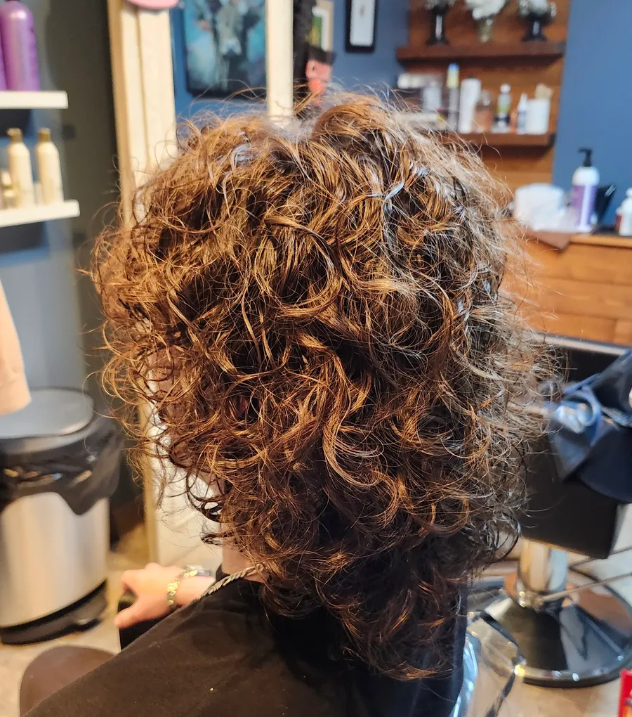 Fresh brunette perm curls with dimension, photographed from behind at the styling chair