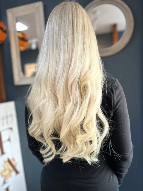 Long platinum blonde hair in soft waves, seen from behind in the salon
